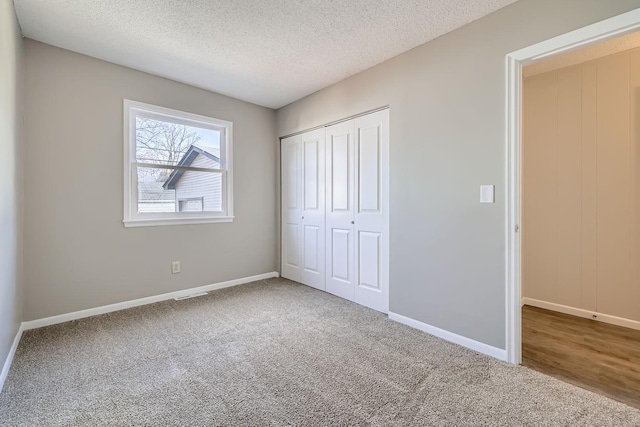 unfurnished bedroom featuring carpet, a closet, visible vents, a textured ceiling, and baseboards