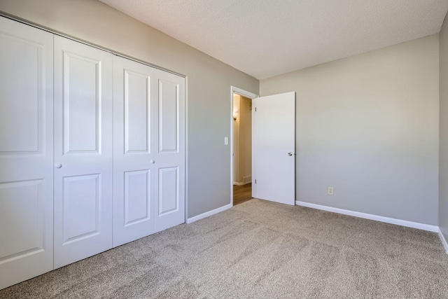 unfurnished bedroom with carpet floors, a closet, a textured ceiling, and baseboards