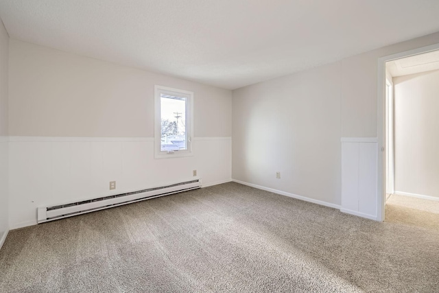 spare room featuring a baseboard heating unit, carpet, and a wainscoted wall