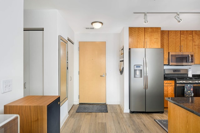 929 Portland Ave Unit 309, Minneapolis, MN 55404 - kitchen with appliances with stainless steel finishes, brown cabinets, light wood-type flooring, rail lighting, and dark stone counters