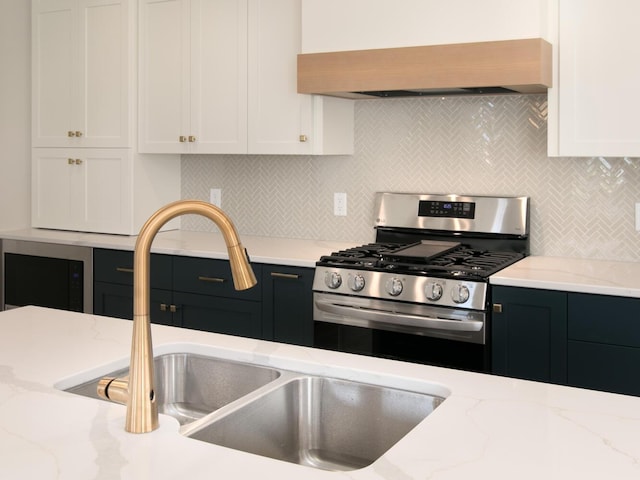 kitchen with stainless steel gas range oven, decorative backsplash, white cabinets, premium range hood, and a sink