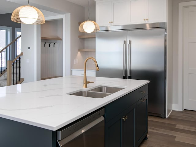 kitchen with a sink, appliances with stainless steel finishes, dark wood-style floors, open shelves, and a center island with sink