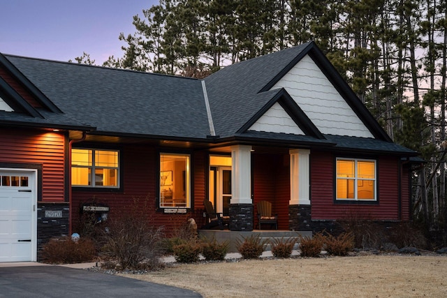 view of front of home featuring an attached garage, covered porch, and a shingled roof