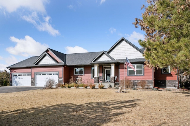 craftsman-style home with a porch, an attached garage, stone siding, and driveway