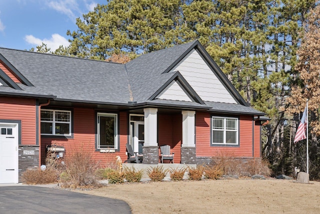 view of front facade with a porch, a garage, roof with shingles, and aphalt driveway