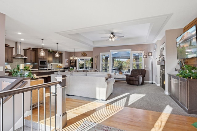 living room with a tray ceiling, a warm lit fireplace, recessed lighting, baseboards, and ceiling fan