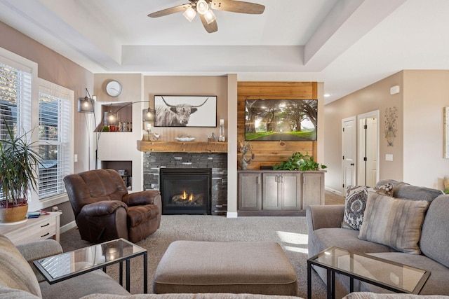 living area featuring a glass covered fireplace, carpet, a raised ceiling, and ceiling fan