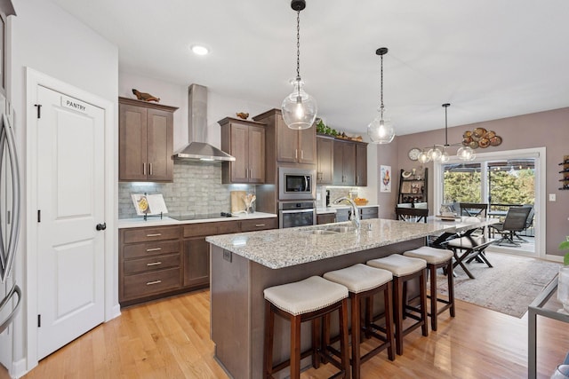 kitchen featuring a sink, backsplash, stainless steel appliances, a breakfast bar area, and wall chimney exhaust hood