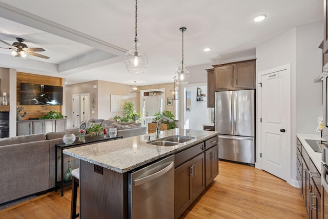 kitchen featuring light wood finished floors, ceiling fan, open floor plan, appliances with stainless steel finishes, and a sink