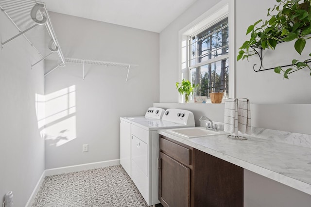 clothes washing area featuring washer and clothes dryer, cabinet space, baseboards, and a sink