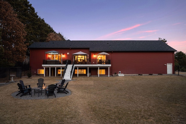 rear view of property featuring a lawn, stairway, a fire pit, a shingled roof, and a wooden deck