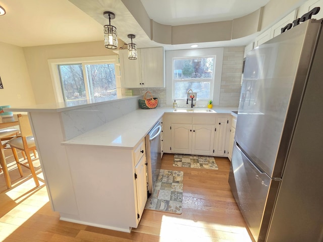 kitchen with a peninsula, a sink, stainless steel appliances, light wood-style floors, and backsplash