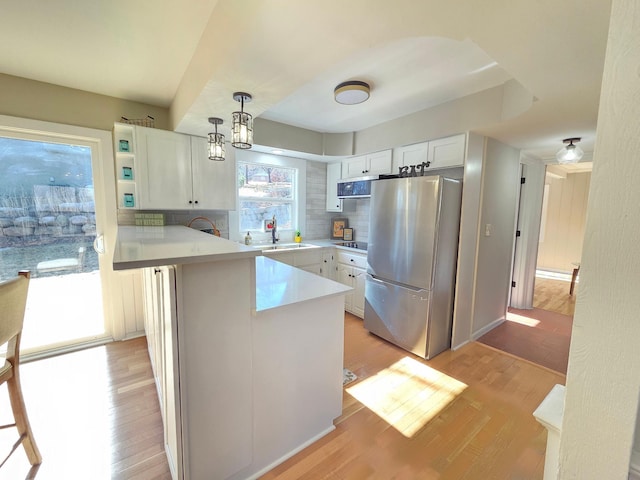 kitchen with light wood-style flooring, appliances with stainless steel finishes, a peninsula, a sink, and backsplash