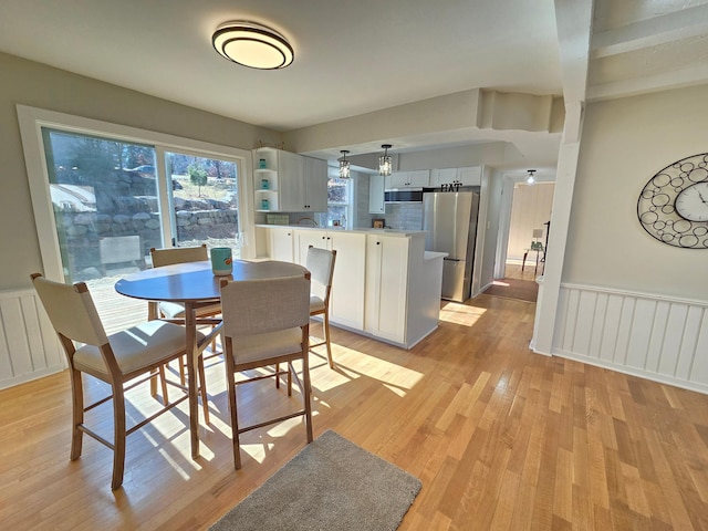 dining space featuring wainscoting, a decorative wall, and light wood finished floors