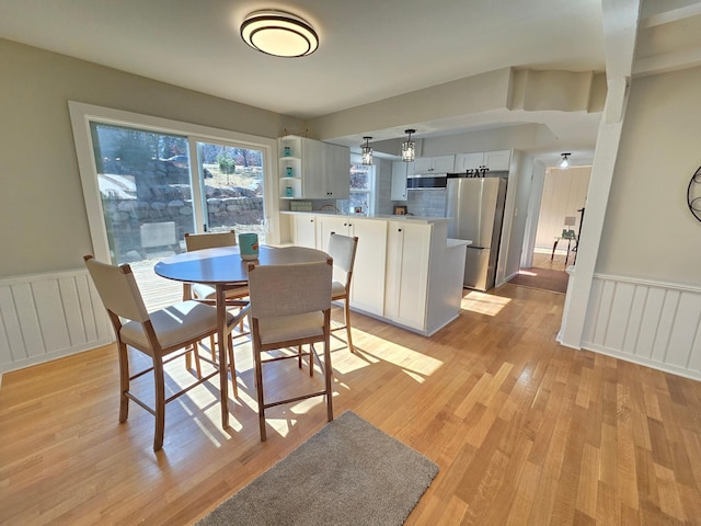 dining area featuring a wainscoted wall, light wood-style flooring, and radiator heating unit