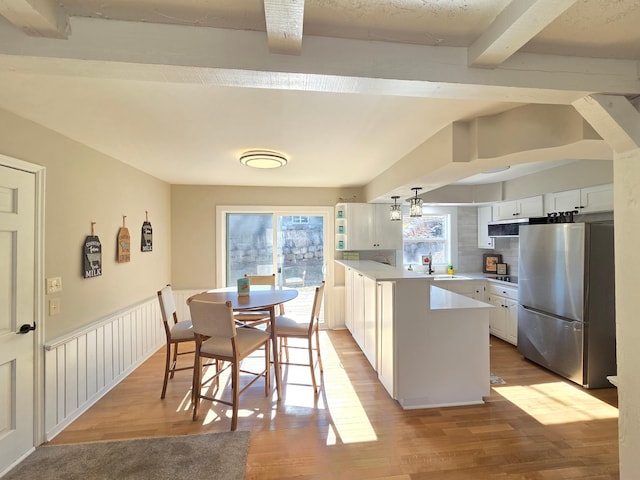 kitchen with light countertops, light wood-style floors, freestanding refrigerator, wainscoting, and a peninsula