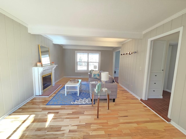 living room with ornamental molding, a glass covered fireplace, beam ceiling, and light wood-style flooring