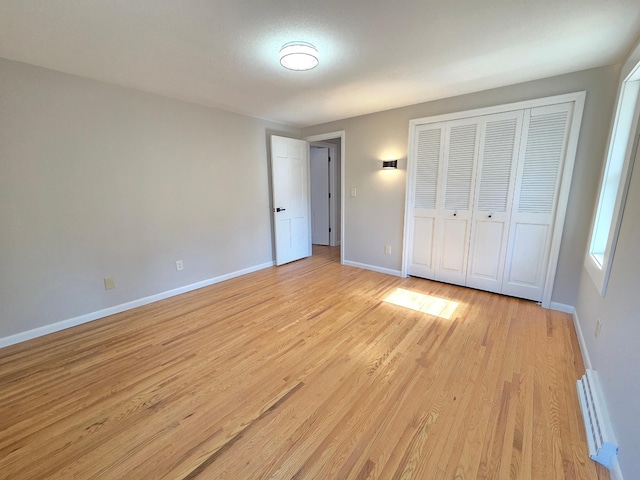 unfurnished bedroom with light wood-type flooring, a baseboard radiator, baseboards, and a closet