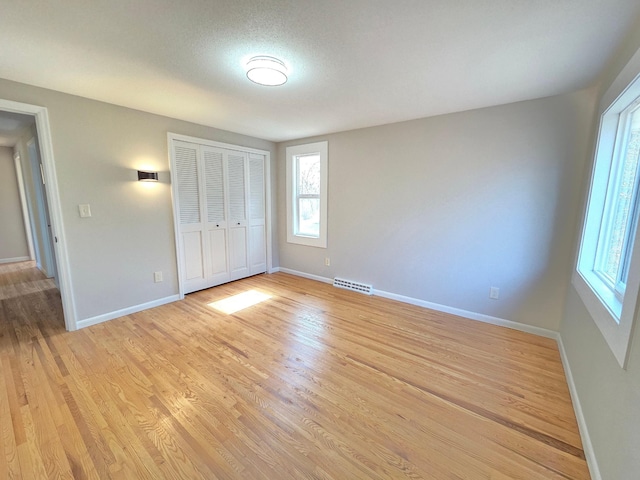 unfurnished bedroom featuring light wood finished floors, baseboards, visible vents, a textured ceiling, and a closet