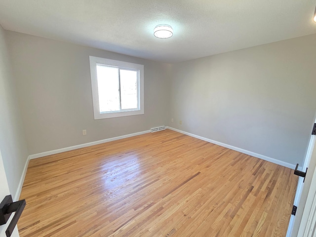 empty room featuring light wood finished floors, visible vents, and baseboards