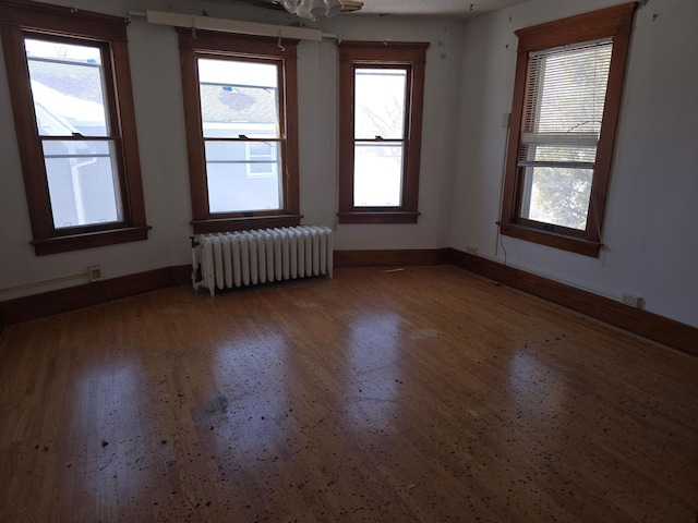 unfurnished room featuring baseboards, wood finished floors, and radiator