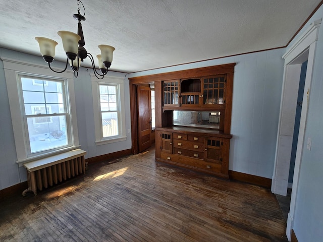 unfurnished dining area featuring a textured ceiling, dark wood-type flooring, baseboards, radiator, and an inviting chandelier