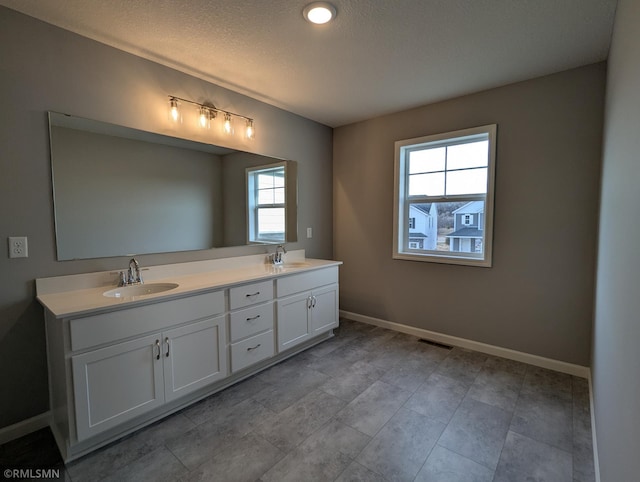 bathroom featuring double vanity, a textured ceiling, baseboards, and a sink