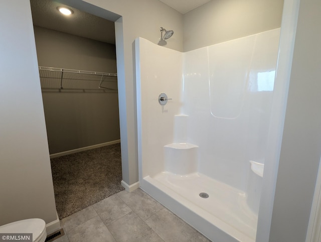 full bath with toilet, tile patterned flooring, baseboards, walk in shower, and a spacious closet