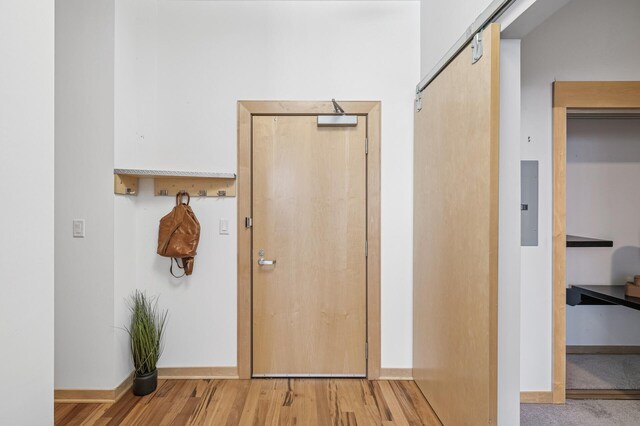 corridor with wood finished floors, electric panel, baseboards, and a barn door