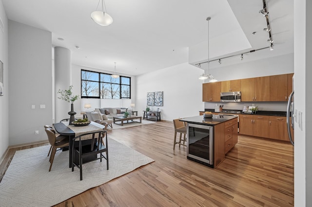 kitchen with beverage cooler, brown cabinetry, dark countertops, light wood-style flooring, and stainless steel microwave