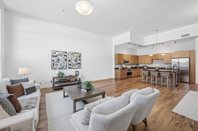 living area featuring baseboards, visible vents, a towering ceiling, light wood-type flooring, and track lighting