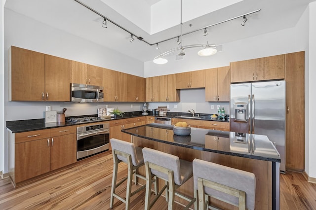 kitchen with light wood finished floors, stainless steel appliances, brown cabinetry, a sink, and a kitchen bar