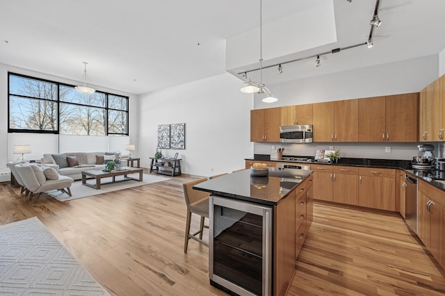 kitchen featuring wine cooler, stainless steel appliances, light wood-style floors, brown cabinetry, and dark countertops