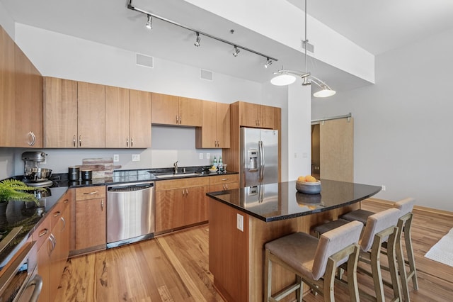 kitchen with a barn door, a sink, a kitchen breakfast bar, appliances with stainless steel finishes, and light wood-type flooring