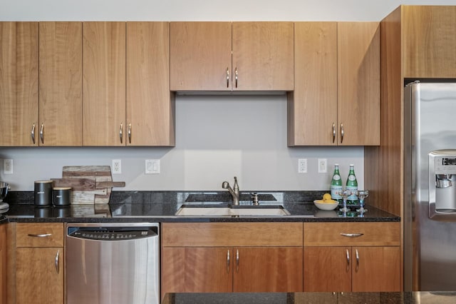 kitchen featuring stainless steel appliances, brown cabinets, a sink, and dark stone countertops