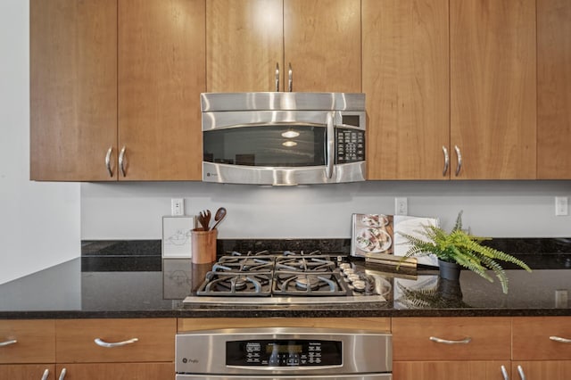 kitchen with gas cooktop, wall oven, brown cabinets, stainless steel microwave, and dark stone countertops