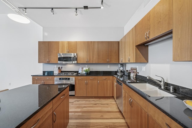 kitchen with stainless steel appliances, brown cabinets, a sink, and light wood-style flooring