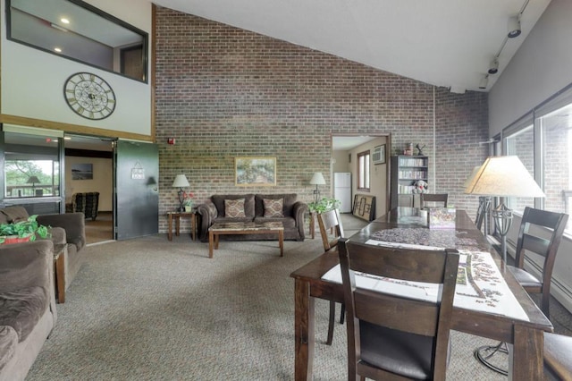 carpeted dining area featuring high vaulted ceiling, brick wall, and rail lighting