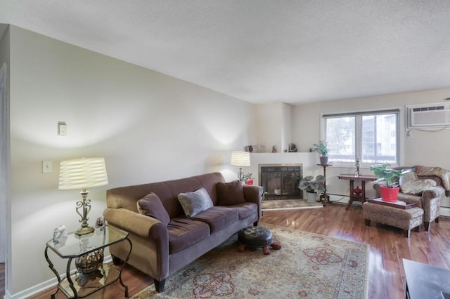 living area featuring a fireplace with raised hearth, a textured ceiling, wood finished floors, baseboards, and an AC wall unit