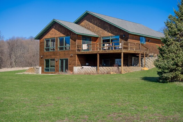 back of property with a wooden deck, roof with shingles, and a yard