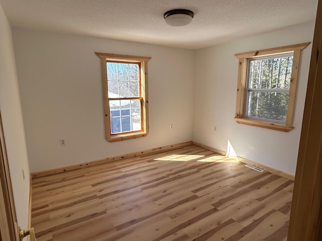 unfurnished room featuring light wood-type flooring, baseboards, and a textured ceiling