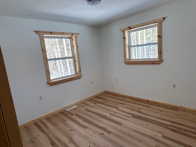 spare room featuring visible vents, baseboards, light wood finished floors, and a textured ceiling