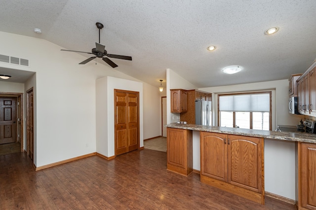 kitchen featuring visible vents, brown cabinetry, lofted ceiling, dark wood-style floors, and stainless steel appliances