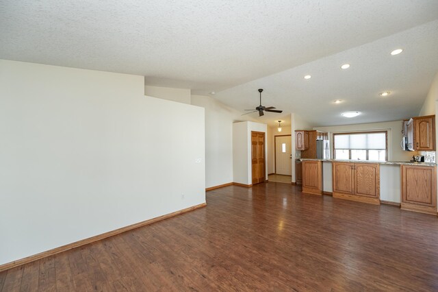 unfurnished living room featuring baseboards, ceiling fan, dark wood-style flooring, and vaulted ceiling