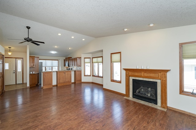 unfurnished living room with a textured ceiling, lofted ceiling, dark wood-type flooring, and a tile fireplace