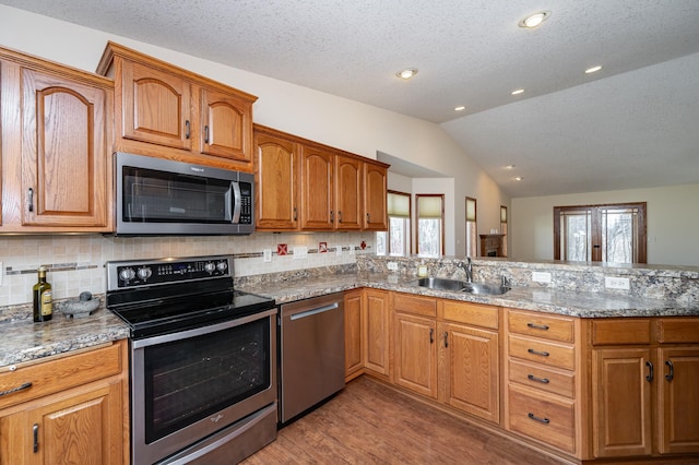 kitchen featuring lofted ceiling, decorative backsplash, light wood-style flooring, stainless steel appliances, and a sink