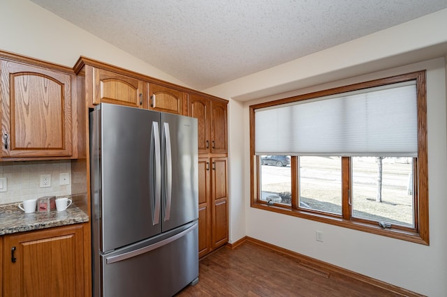 kitchen featuring dark wood-style flooring, freestanding refrigerator, vaulted ceiling, brown cabinets, and backsplash