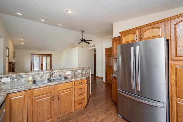 kitchen with a sink, light stone counters, appliances with stainless steel finishes, and vaulted ceiling