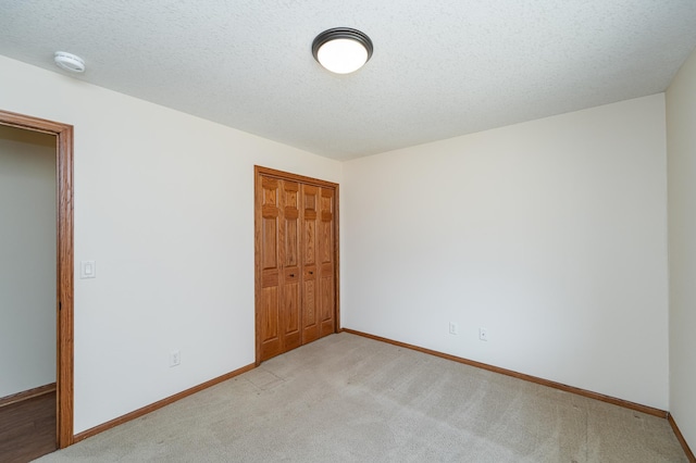 unfurnished bedroom featuring a closet, light carpet, a textured ceiling, and baseboards