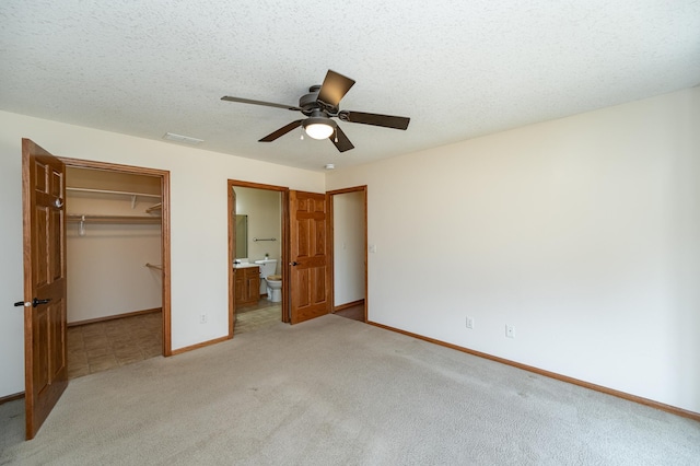 unfurnished bedroom featuring a textured ceiling, baseboards, a spacious closet, a closet, and light carpet